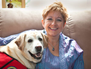 Photo of Dr. Betz King and her dog, a yellow lab named Paisley, wearing a red therapy dog vest.