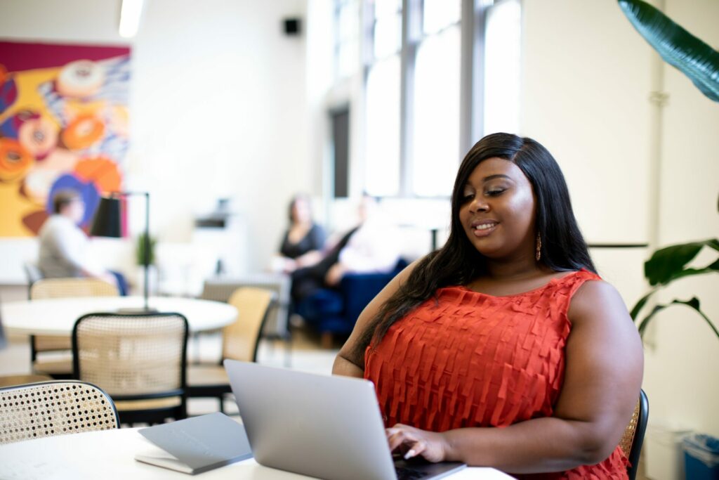 Stock photo of a women working on a laptop with a journal sitting on the table next to her