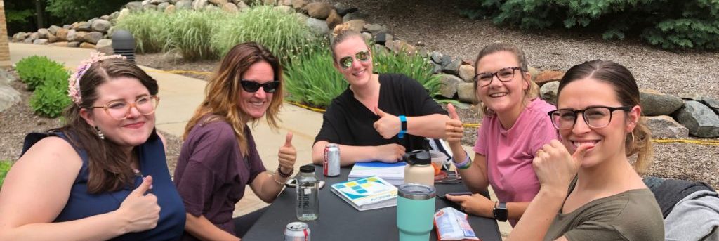 Students giving a thumbs up while sitting at a table studying outside