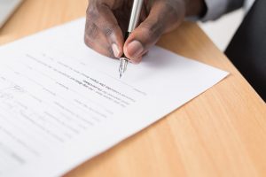 Photo of a person's hand holding a pen and signing a document. 