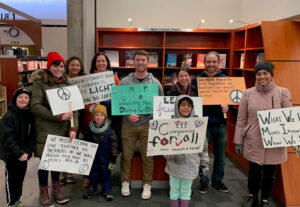Group photo of MSP community members holding signs and standing in front of a bookshelf