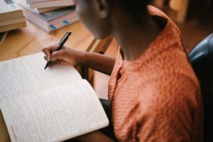 Photo from above of a person writing in a notebook. Face is not visible.