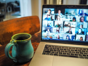Photo of a laptop showing an online conference on the screen with a coffee cup sitting next to it on the table