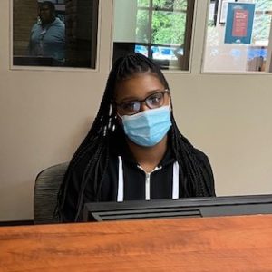 Photo of Cierra Fitzgerald wearing a mask and sitting at the front desk