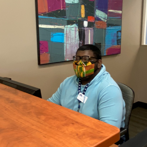Photo of Dennis Brown, wearing a mask and sitting at the front desk