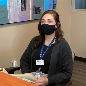 Photo of Erin Stockwell wearing a mask and sitting at the front desk