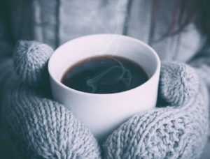 Photo up close of hands in mittens holding coffee.