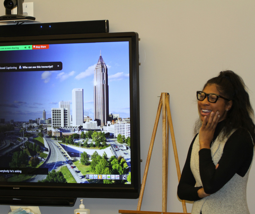 Dr. Erin White standing and smiling in front of a presentation that features the Detroit skyline.