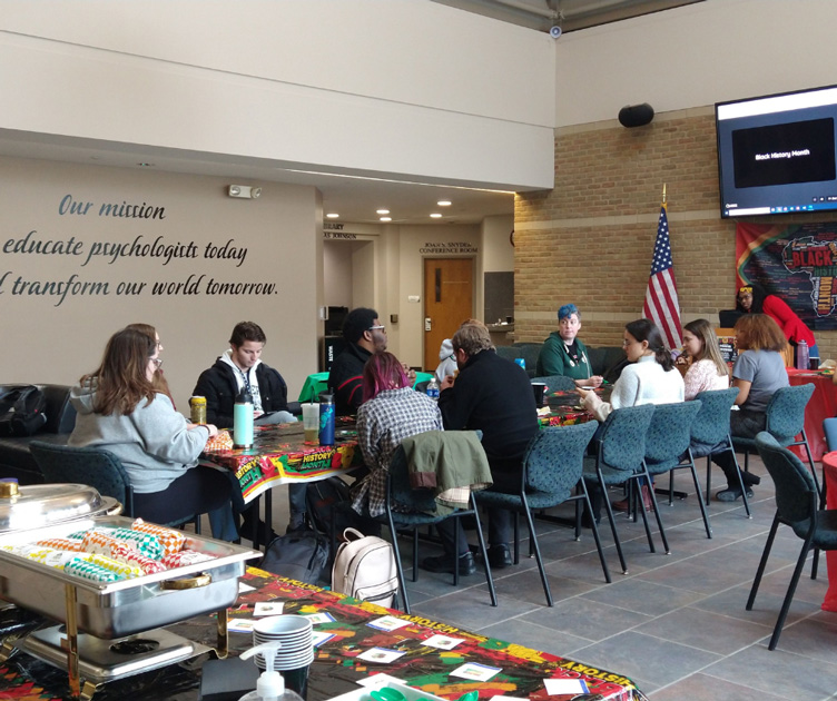 Students and faculty sitting at a long table decorated with a Black History Month table cloth and catered breakfast appears in the background.