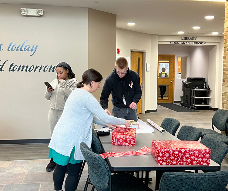 Two students and a staff member at a table wrapping gifts.