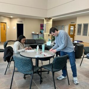 Female student and male staff member at a table wrapping and labeling gifts for adopt a family