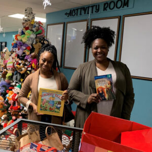 First year doctoral students Sharmane Brown and Ashley Craft holding books in front of the activity room at the center