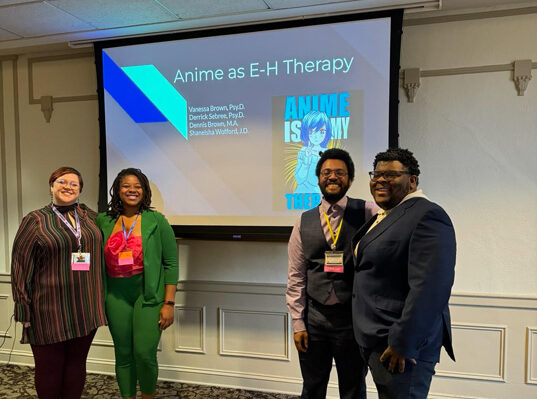 Dr. Brown, Shaneisha Wofford, Dr. Sebree, and Dennis pose with a slide that reads Anime as E-H Therapy.