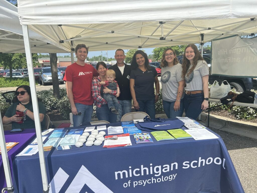 Photo of students and staff standing behind a table with information pamphlets displayed.
