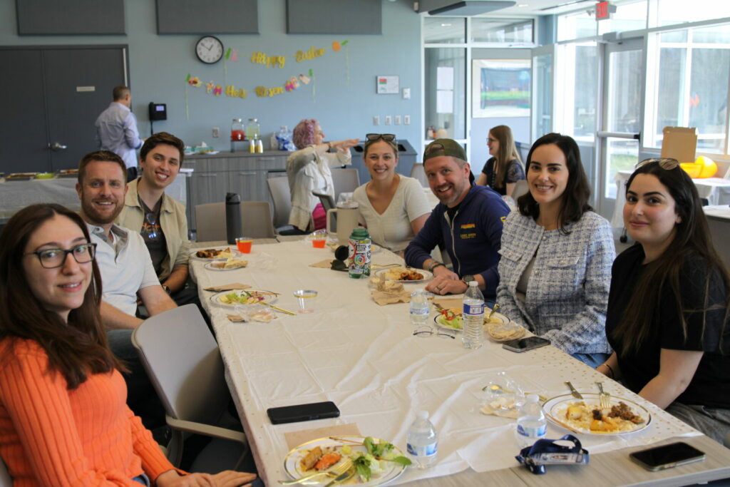 Students faculty and staff sitting at a lunch table posing for the camera.