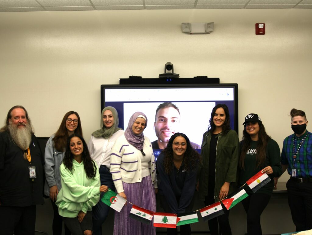 Photo of staff and students in the MENAPC holding a banner feature different MENA flags.
