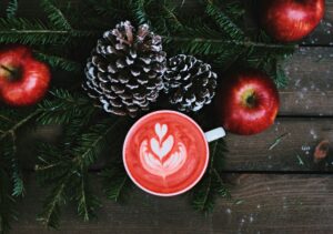 Mug with latte art with a winter background featuring pine cones, apples, and tree branches on a wooden table