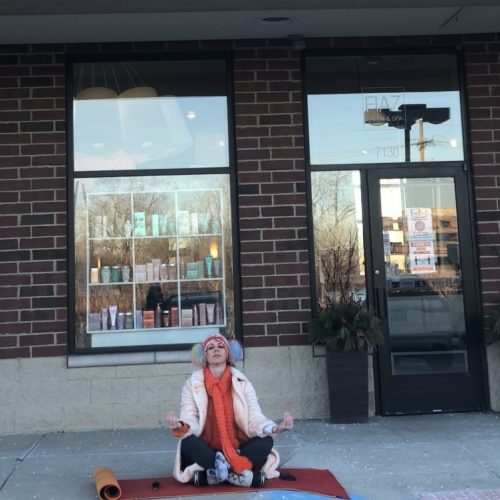 Photo of a student meditating on a yoga mat outside of a storefront